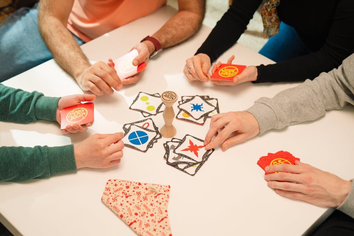 Handen rond de houten totem van Jungle Speed op een witte tafel